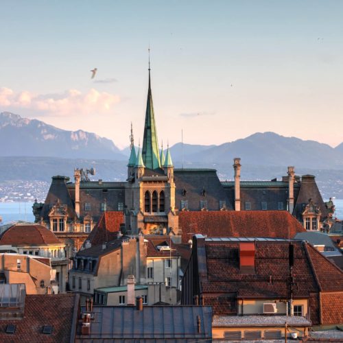 Skyline of Lausanne, Switzerland as seen from the Cathedral hill at sunset zoomed-in on the tower of St-Francois Church. Lake Leman (Lake Geneva) and the French Alps provide a beautiful background.